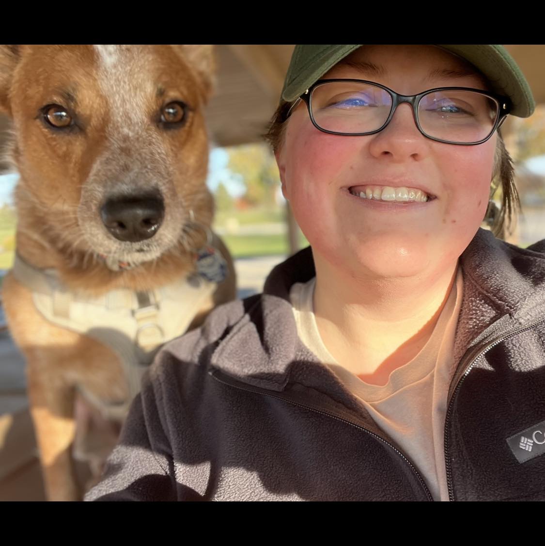 Brittany Hicks smiling next to her red heeler mix dog on a sunny day.